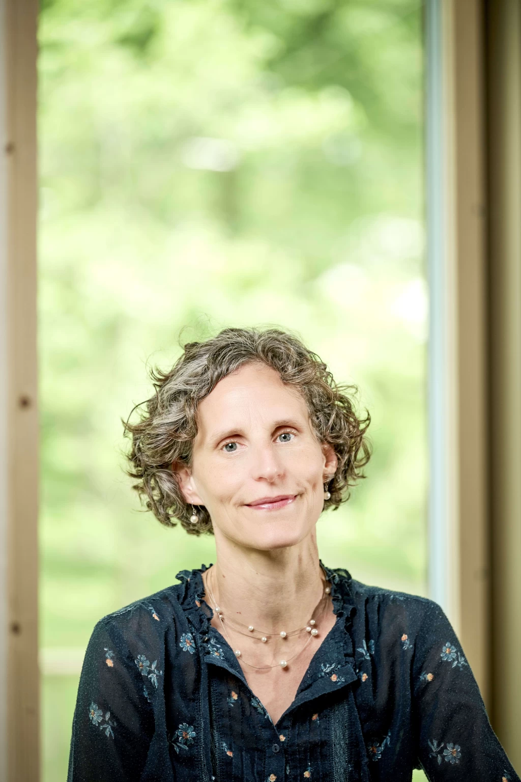 Portrait of Andrea Schärli in front of a large window with greenery in the background.