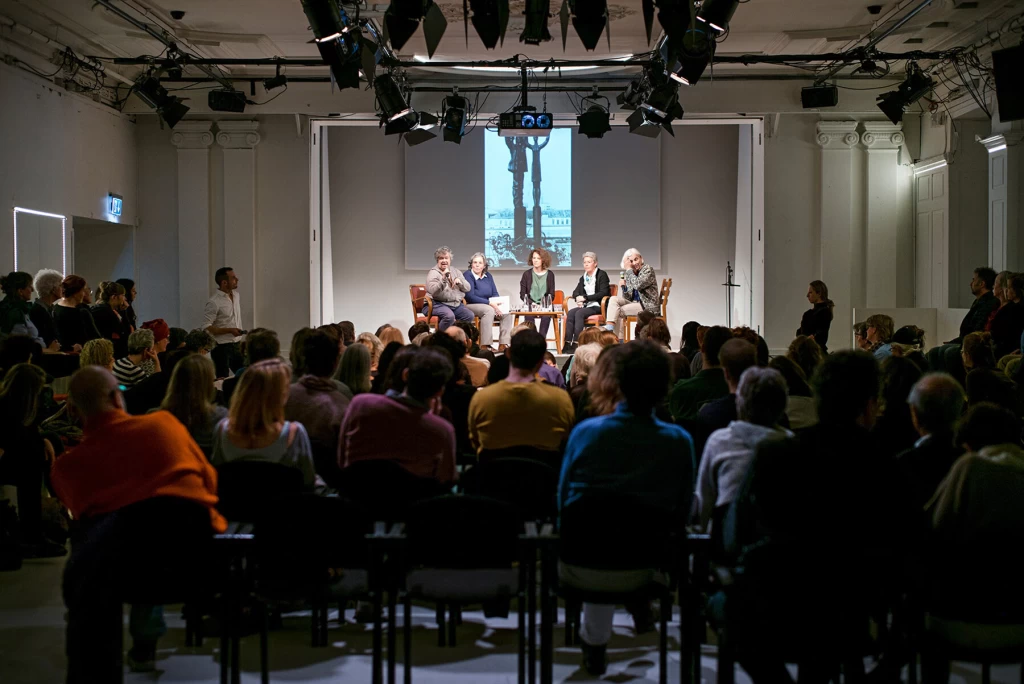 Well-attended panel discussion with five people on stage and an audience in the hall.