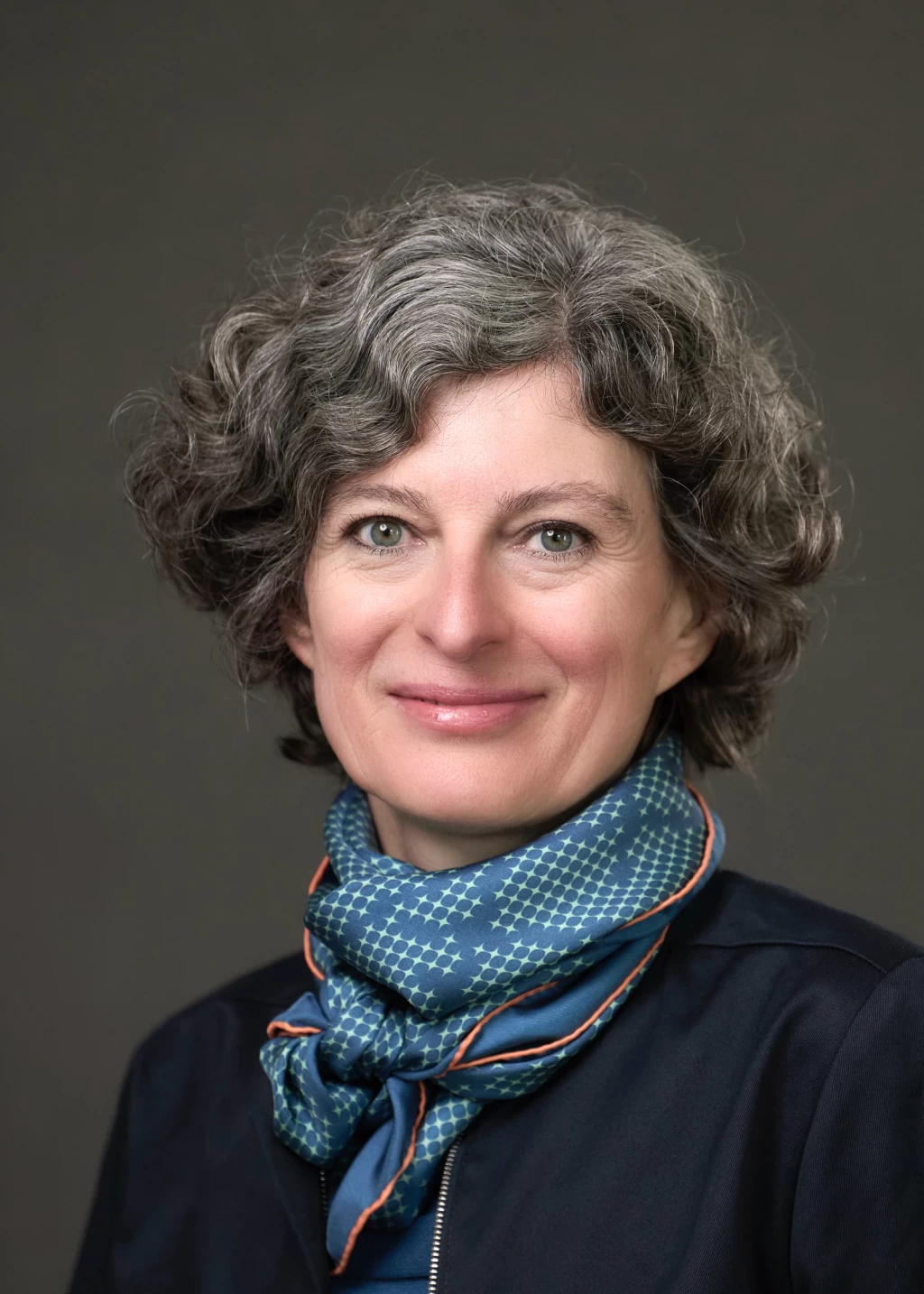 Christina Thurner sitting cross-legged on a bench in front of a blue wall.