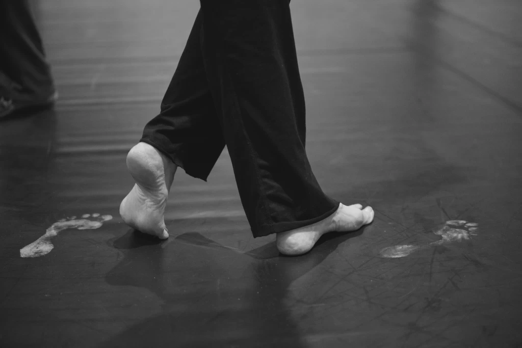 Close-up of bare feet in motion on a dance floor, with visible footprints nearby.