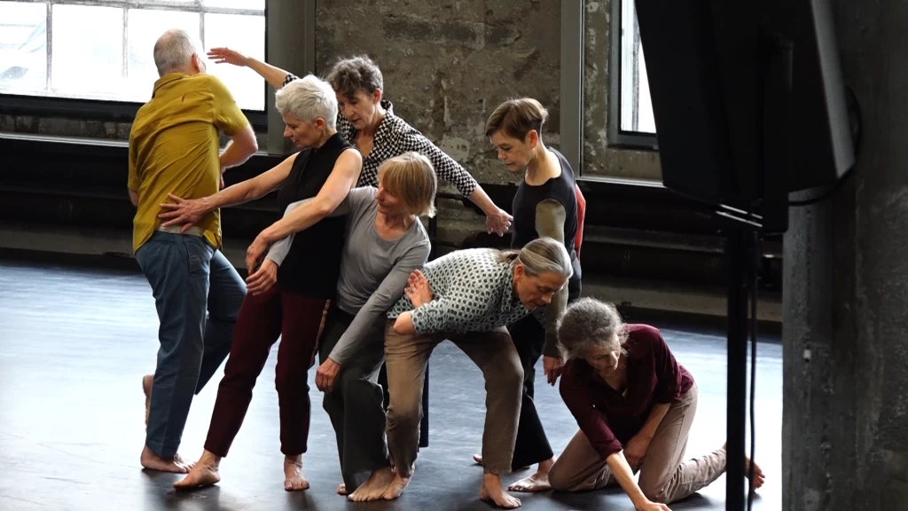 Group of older dancers in different movement positions in a dance studio.