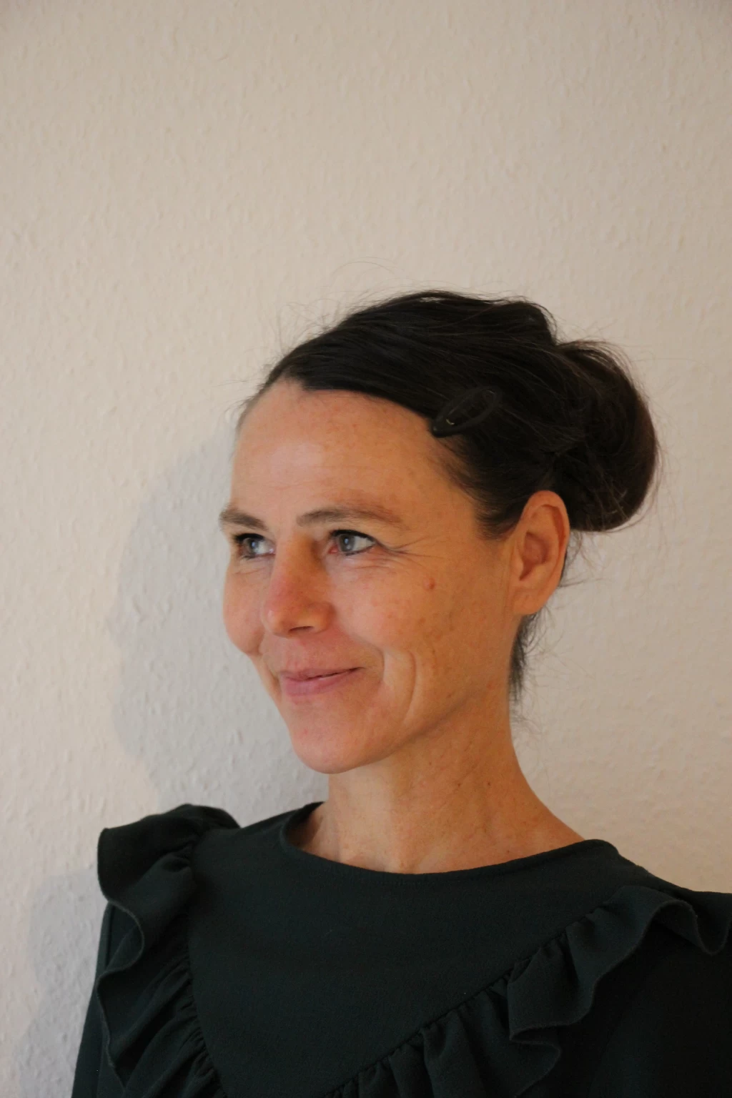 Portrait of Jutta Krauss with her hair pinned up against a light wall.