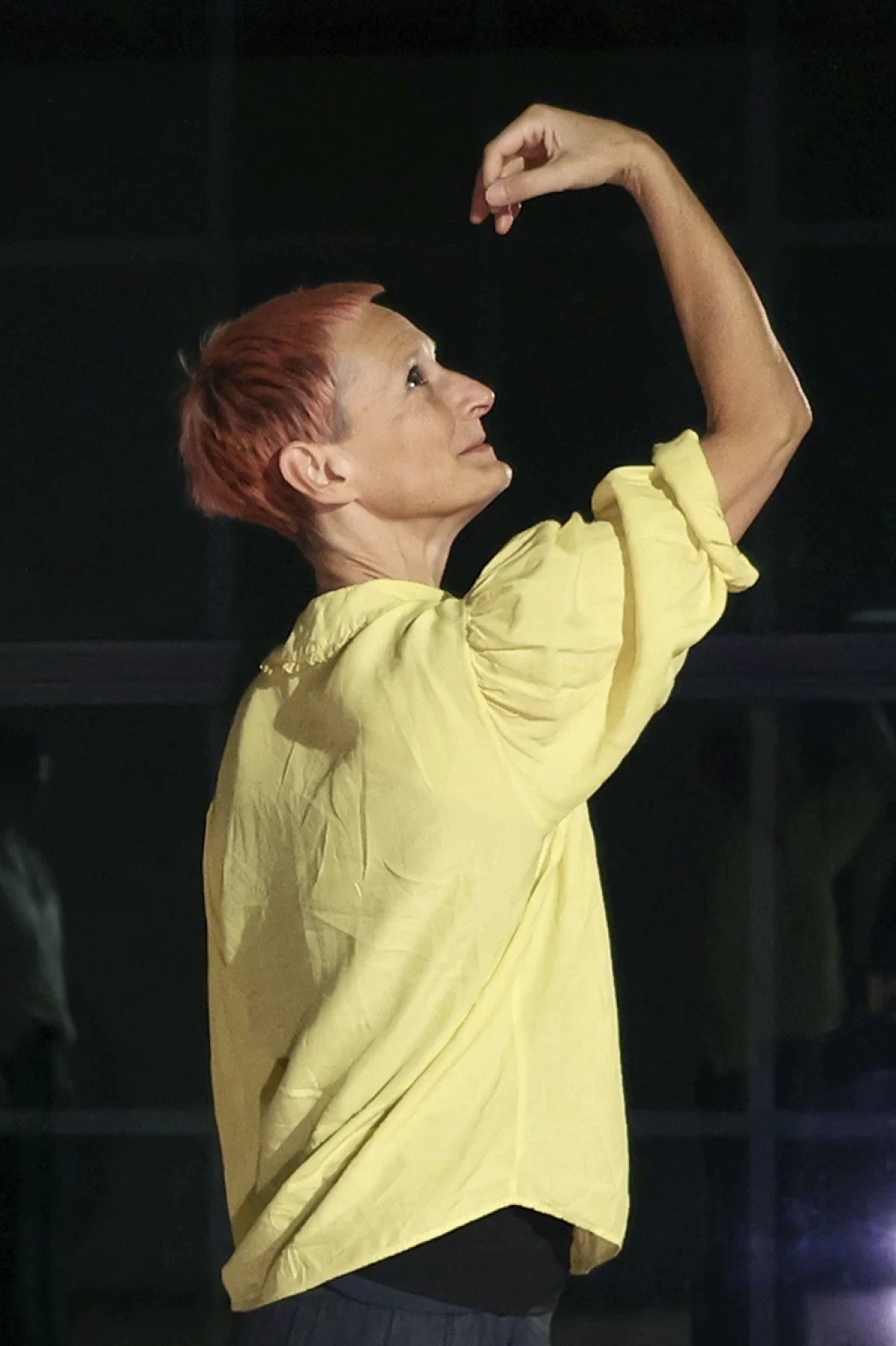 Susanne Martin wearing a yellow top and raising one arm above her head.
